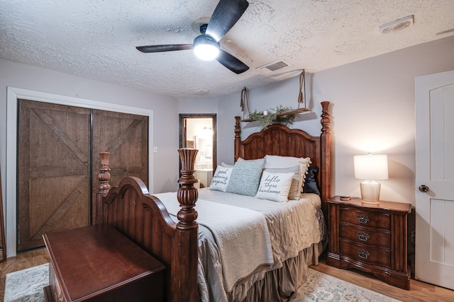 bedroom featuring visible vents, light wood-style floors, a textured ceiling, ensuite bath, and a ceiling fan