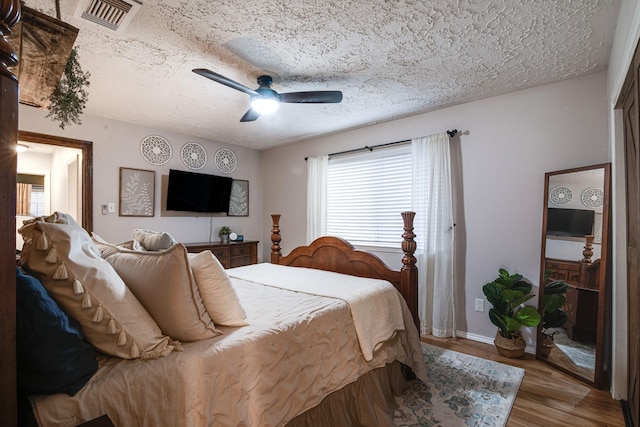 bedroom featuring a ceiling fan, baseboards, wood finished floors, visible vents, and a textured ceiling