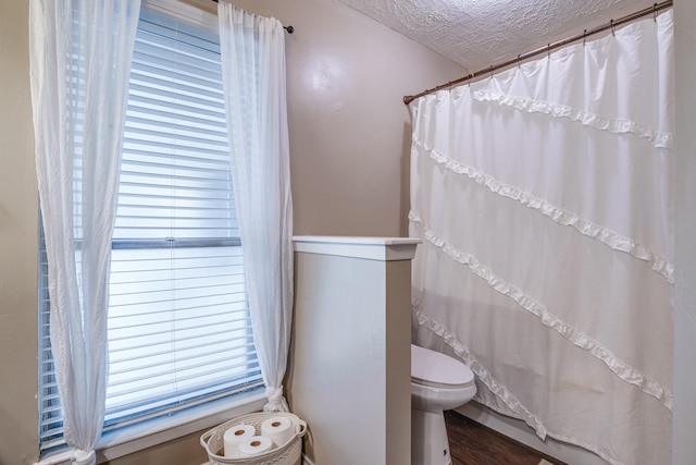 full bath with a shower with shower curtain, toilet, wood finished floors, and a textured ceiling