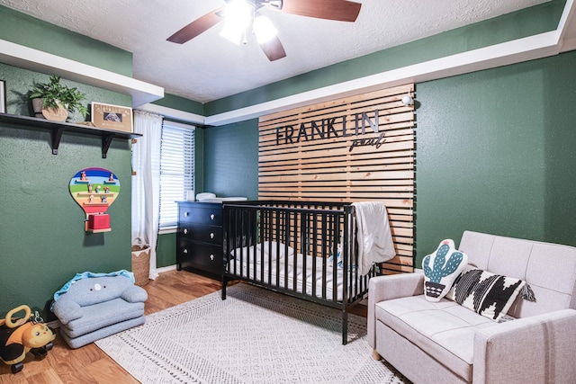 bedroom featuring a nursery area, wood finished floors, and a textured wall