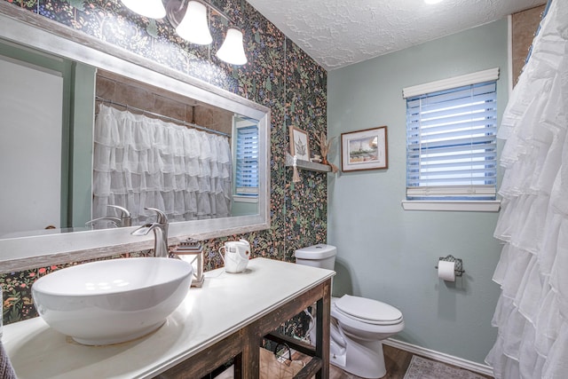 bathroom with toilet, a textured ceiling, wallpapered walls, baseboards, and vanity