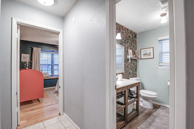 bathroom with a textured ceiling, toilet, baseboards, and wood finished floors