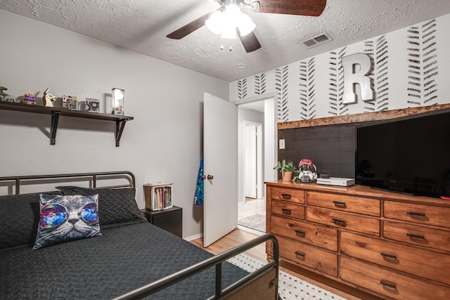 bedroom featuring light wood-style floors, visible vents, a textured ceiling, and ceiling fan