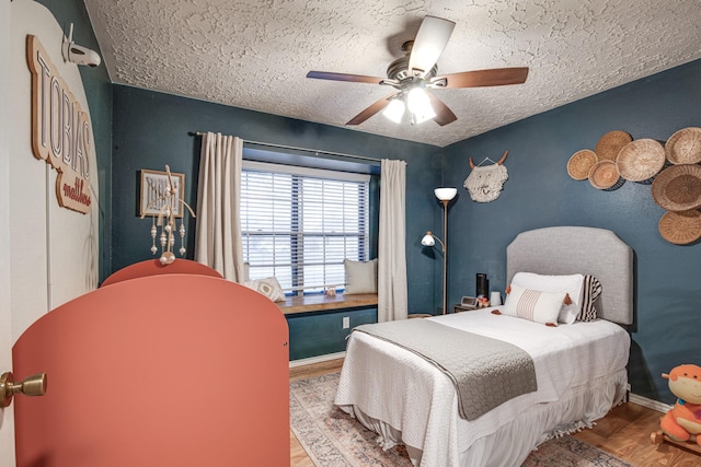 bedroom with ceiling fan, wood finished floors, baseboards, and a textured ceiling