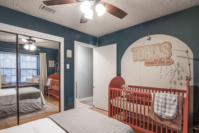 bedroom featuring visible vents, a crib, a ceiling fan, a textured ceiling, and a closet