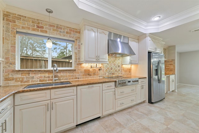 kitchen featuring a sink, appliances with stainless steel finishes, wall chimney exhaust hood, a tray ceiling, and tasteful backsplash