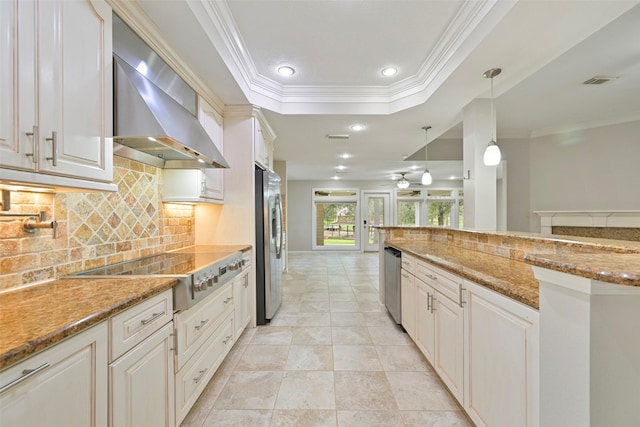 kitchen featuring a tray ceiling, stainless steel appliances, visible vents, ornamental molding, and wall chimney exhaust hood