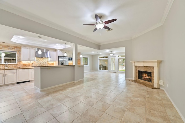 kitchen featuring a raised ceiling, appliances with stainless steel finishes, open floor plan, ceiling fan, and wall chimney range hood