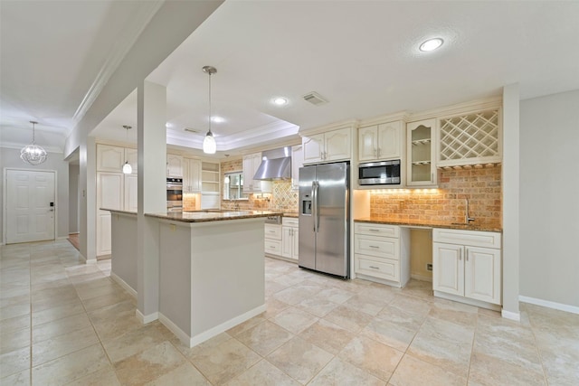 kitchen with visible vents, cream cabinetry, appliances with stainless steel finishes, wall chimney exhaust hood, and a tray ceiling