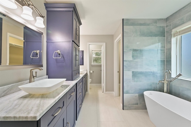 bathroom with baseboards, toilet, tile patterned floors, vanity, and a freestanding tub