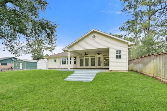 back of house with fence, a lawn, a ceiling fan, and an outdoor structure