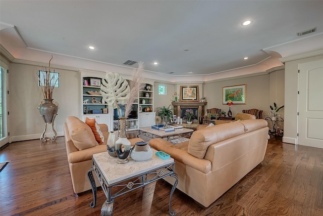 living area with crown molding, visible vents, a fireplace with raised hearth, and wood finished floors