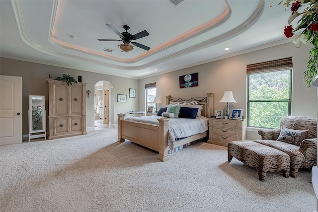 bedroom featuring arched walkways, a tray ceiling, light carpet, and crown molding