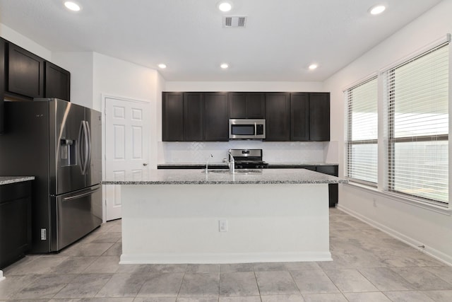 kitchen with stainless steel appliances, visible vents, decorative backsplash, a sink, and an island with sink