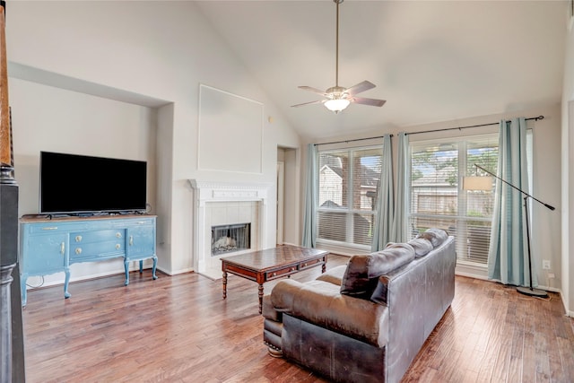 living area with high vaulted ceiling, light wood-type flooring, ceiling fan, and a tiled fireplace