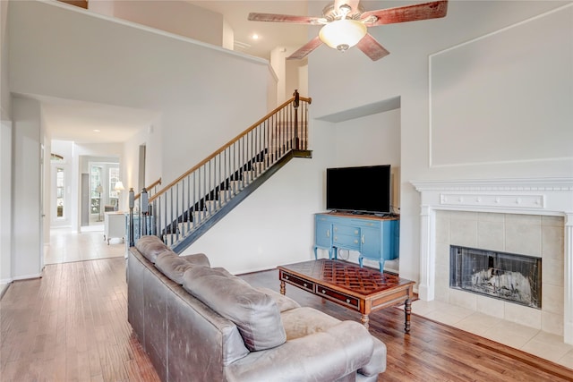 living area featuring ceiling fan, hardwood / wood-style flooring, baseboards, stairway, and a tiled fireplace