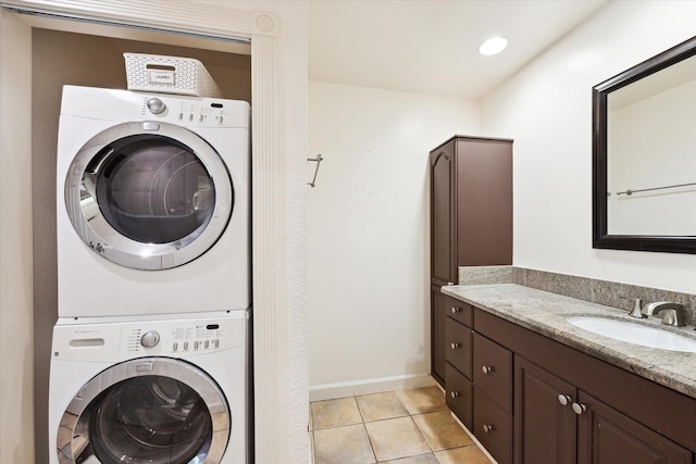 clothes washing area featuring light tile patterned floors, stacked washer and dryer, laundry area, a sink, and baseboards