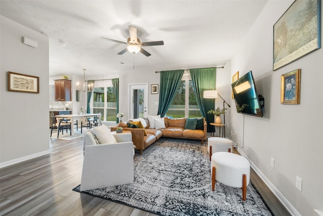 living room with baseboards, wood finished floors, and ceiling fan with notable chandelier