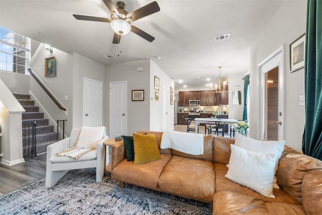 living area featuring ceiling fan with notable chandelier, stairway, wood finished floors, and visible vents