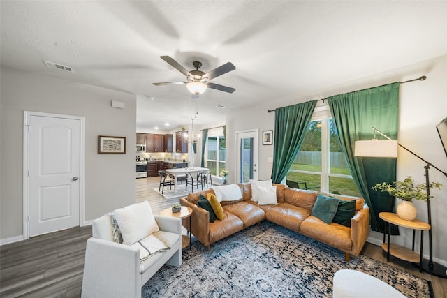 living room featuring ceiling fan with notable chandelier, wood finished floors, visible vents, and baseboards