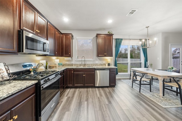 kitchen with light wood-type flooring, visible vents, a sink, light stone counters, and stainless steel appliances