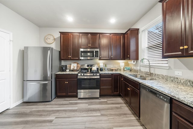 kitchen with light stone counters, a sink, dark brown cabinets, appliances with stainless steel finishes, and light wood-type flooring