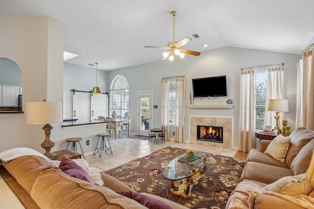 living room featuring light tile patterned floors, a ceiling fan, visible vents, a fireplace, and vaulted ceiling