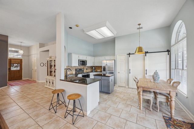 kitchen with dark countertops, a peninsula, light tile patterned flooring, appliances with stainless steel finishes, and a barn door