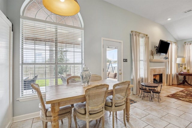 dining room with light tile patterned floors, baseboards, visible vents, lofted ceiling, and a tiled fireplace