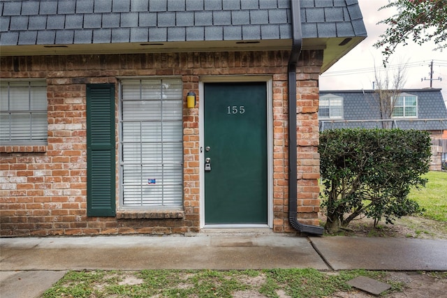 entrance to property with mansard roof, roof with shingles, and brick siding