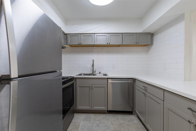 kitchen featuring tasteful backsplash, stainless steel appliances, a sink, and gray cabinetry