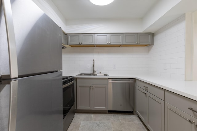 kitchen with backsplash, stainless steel appliances, a sink, and gray cabinetry