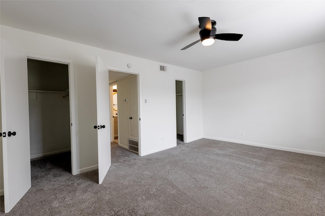 unfurnished bedroom featuring a ceiling fan, a walk in closet, a closet, and carpet flooring