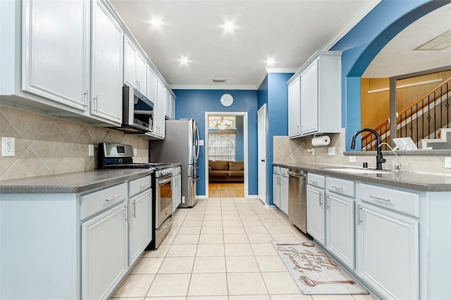 kitchen with light tile patterned floors, dark countertops, appliances with stainless steel finishes, crown molding, and a sink