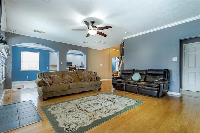 living room with arched walkways, a ceiling fan, visible vents, light wood-type flooring, and crown molding