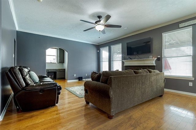 living area featuring arched walkways, ornamental molding, light wood-type flooring, and baseboards