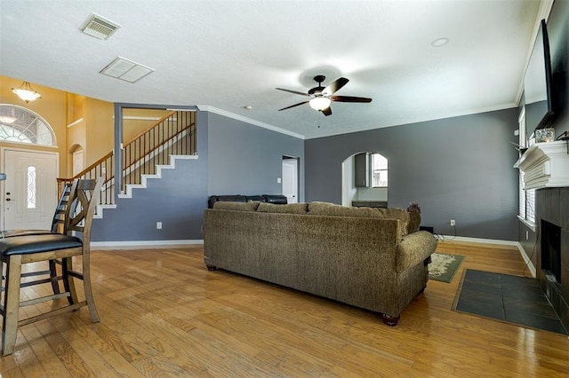 living area with arched walkways, visible vents, stairway, a tiled fireplace, and light wood-type flooring