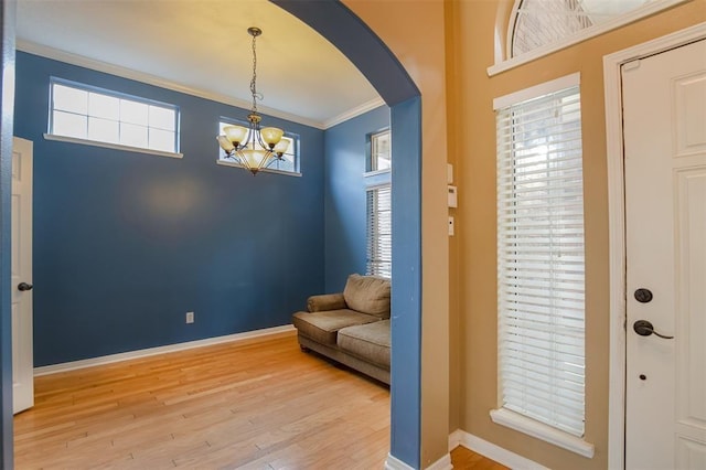 sitting room with baseboards, light wood-style flooring, arched walkways, and crown molding