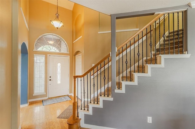 entryway with arched walkways, a high ceiling, wood finished floors, and baseboards