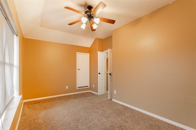 empty room featuring vaulted ceiling, carpet floors, a ceiling fan, and baseboards