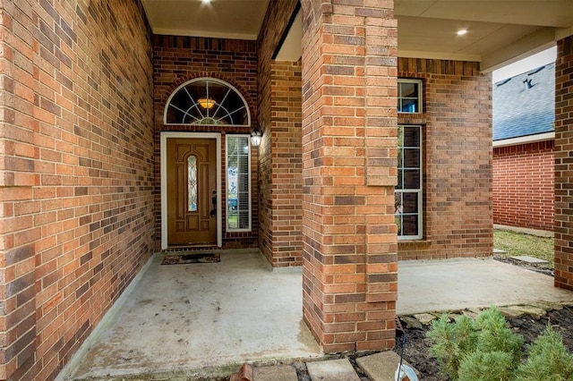 doorway to property with a porch and brick siding