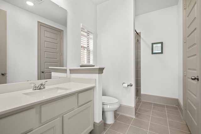 bathroom featuring toilet, vanity, tile patterned flooring, tiled shower, and baseboards