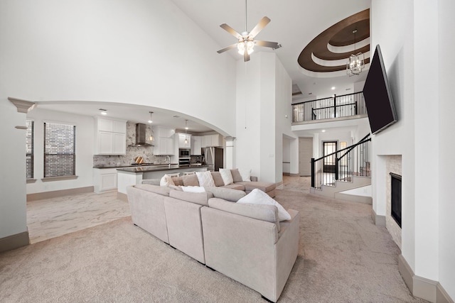 living area featuring arched walkways, light colored carpet, ceiling fan with notable chandelier, stairway, and a glass covered fireplace