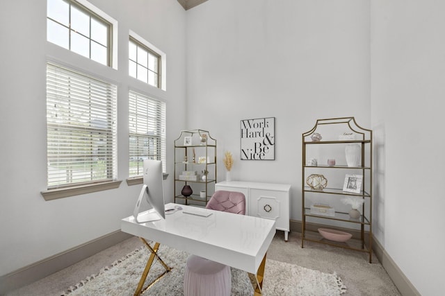 home office with a towering ceiling, baseboards, and light colored carpet