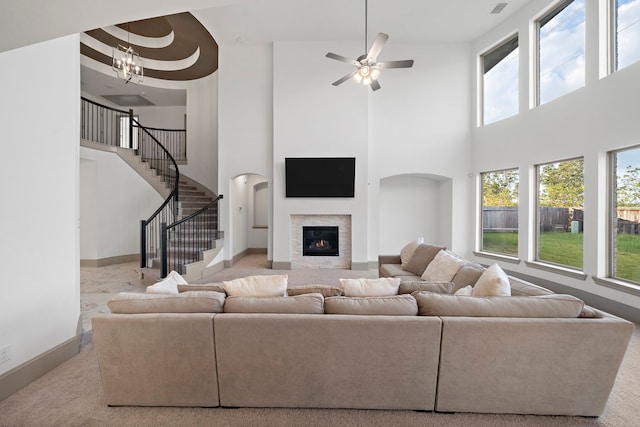 living room with baseboards, ceiling fan with notable chandelier, stairway, and a glass covered fireplace