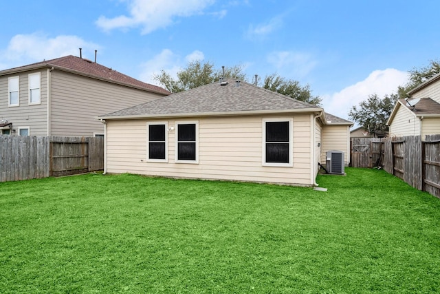 rear view of property featuring a fenced backyard, a lawn, central AC unit, and roof with shingles