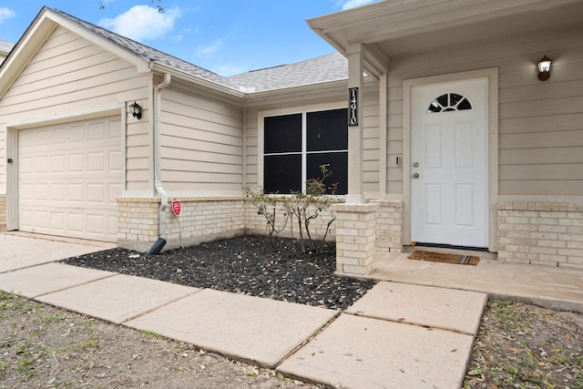 view of exterior entry featuring a garage, a shingled roof, and brick siding