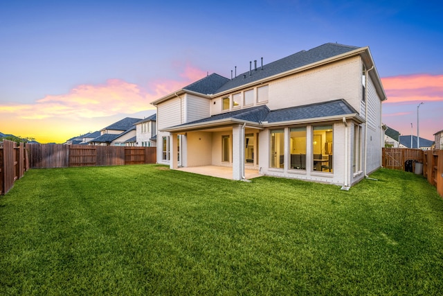 back of property featuring a fenced backyard, roof with shingles, a yard, a patio area, and brick siding