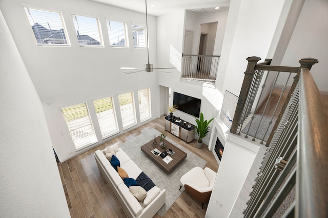 living room featuring a warm lit fireplace, recessed lighting, wood finished floors, a towering ceiling, and a ceiling fan