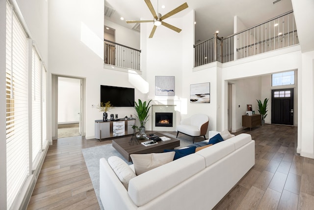 living area featuring a warm lit fireplace, ceiling fan, visible vents, and wood finished floors